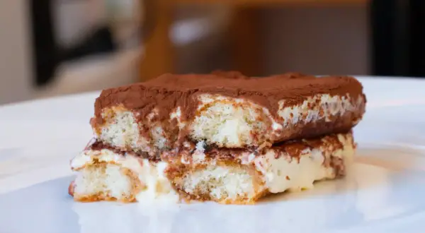 Ein Stück original italienisches Tiramisu, üppig mit Kakao bestäubt, auf einem weißen Teller.