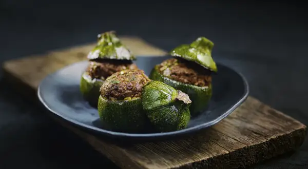 Trois courgettes rondes farcies, garnies d'une préparation savoureuse, reposent sur une assiette sombre, posée sur un plateau en bois vieilli.