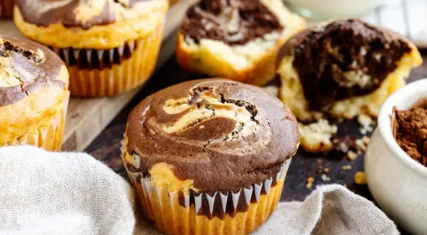 Marmorierte Muffins, perfekt für ein schnelles Muffins Rezept. Ein Muffin ist angeschnitten und zeigt den saftigen Teig.