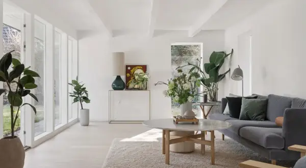 Ein helles, luftiges kleines Wohnzimmer skandinavisch einrichten mit grauem Sofa, Marmortisch und vielen Pflanzen.