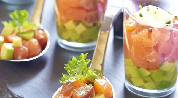 Délicieux tartare saumon fumé avocat servi en verrine et cuillère, garni de ciboulette.