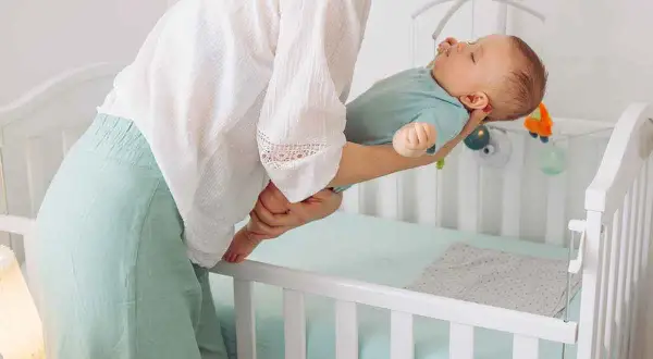 Madre acuna a su bebé dormido, listo para colocarlo en la cuna. Entender las ventanas de sueño es clave para un descanso feliz.