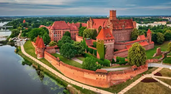 Malbork, najwiekszy zamek w Polsce, majestatycznie wznosi się nad rzeką Nogat, otoczony ceglanymi murami i zielenią.