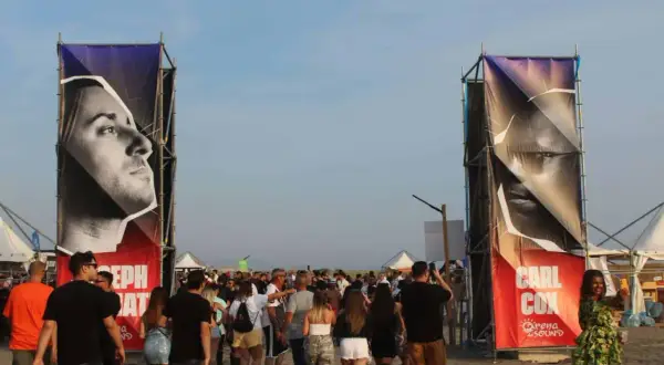 Ingresso per il festival con gigantografie di Carl Cox e Joseph Capriati. La folla si muove sulla sabbia.