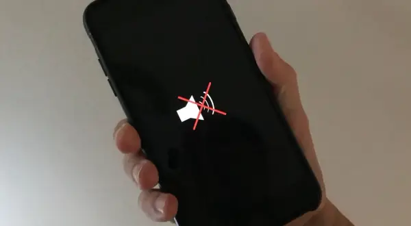 Dłoń trzyma czarny telefon z wyciszonym głośnikiem. Gdy dźwięk nie działa, warto dowiedzieć się, jak wyczyścić głośnik w telefonie.