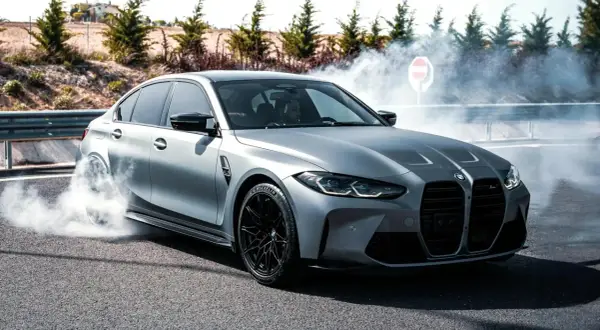 Srebrne BMW M3 G80 w poślizgu, z opon dymiących na asfalcie.