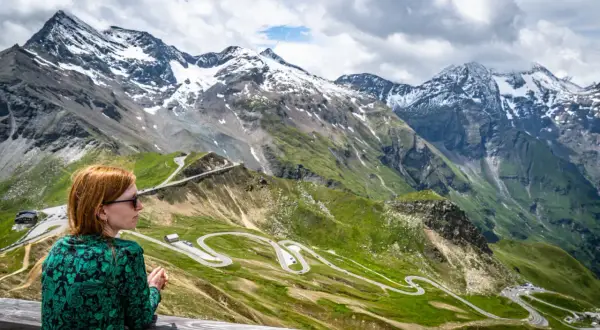 Kobieta podziwia widok na najwyższy szczyt w Austrii. Kręta droga wije się po zielonych zboczach gór.