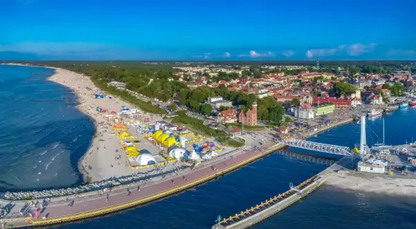 Ustecka plaża tętni życiem, pełna kolorowych namiotów i ludzi. W tle widać urokliwe miasteczko i port. To idealne ustka atrakcje dla każdego.