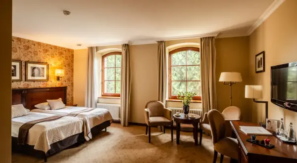 Przytulny pokój hotelowy z dwoma łóżkami, dwoma oknami i widokiem na zieleń. Idealne miejsce na wypoczynek po zwiedzaniu Wrocławia, Zamek Topacz czeka!