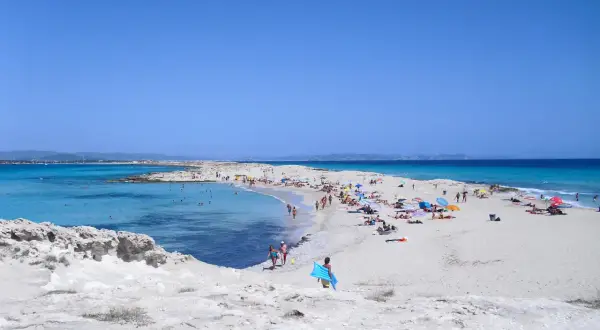 Gente disfrutando de un día soleado en las **playas blancas** con aguas turquesas y cielo azul.
