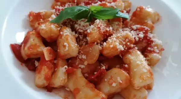 Pyszne gnocchi z sosem pomidorowym, posypane parmezanem i udekorowane listkiem bazylii.