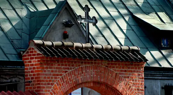 Ceglany łuk i dach kościoła z krzyżem. Nawet apostata mógłby tu znaleźć spokój, patrząc na te dachówki.