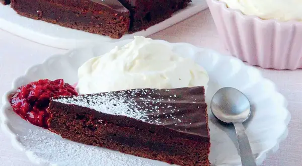 En bit fransk chokladtårta med vispad grädde och hallonsylt. Pudrad med florsocker.