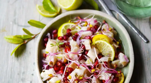 Un délicieux ceviche de poisson frais, garni de grenade, de pousses et de rondelles de citron vert.