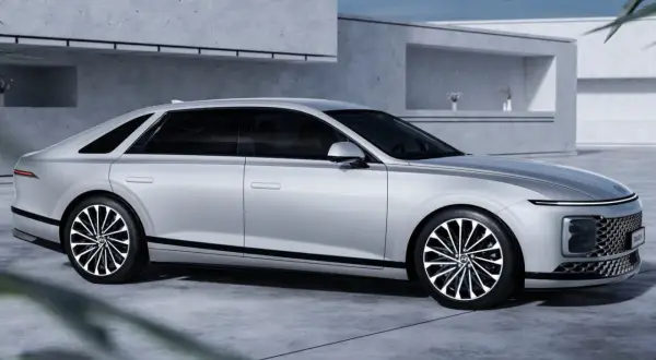 Srebrny Hyundai Grandeur z czarnymi akcentami i felgami stoi przed nowoczesnym budynkiem.