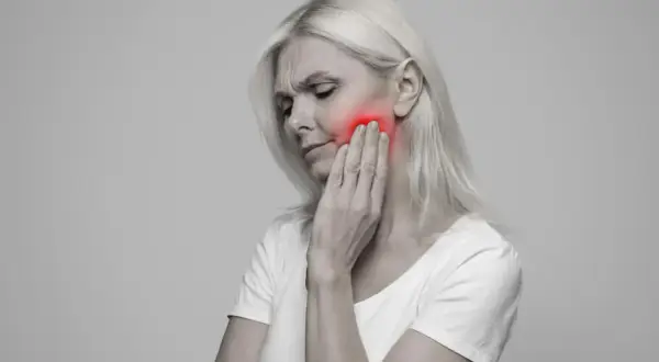 Donna con dolore alla mascella, evidenziato in rosso. Le conseguenze di una mandibola fuori asse possono essere debilitanti.