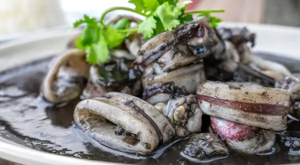 Calamares en su tinta, un plato oscuro y delicioso, adornado con cilantro fresco.