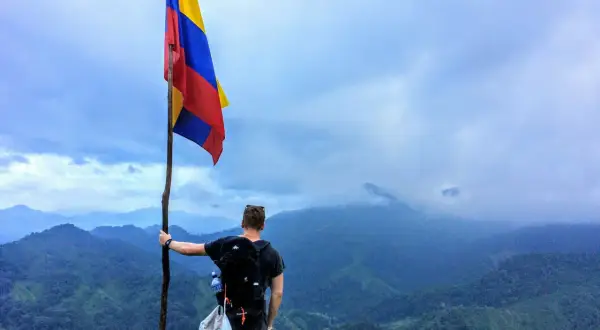 Vandrare med Colombias flagga på en bergstopp. Trots att en resa till Colombia kan verka farligt, bjuder landet på otroliga vyer.