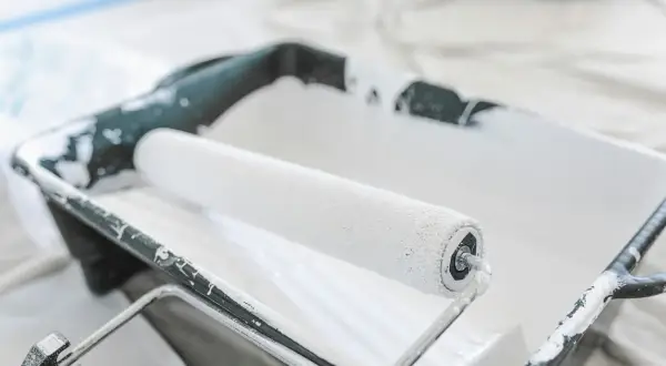 Un rouleau à peinture blanc est posé dans un bac en plastique noir, prêt à enlever la peinture.