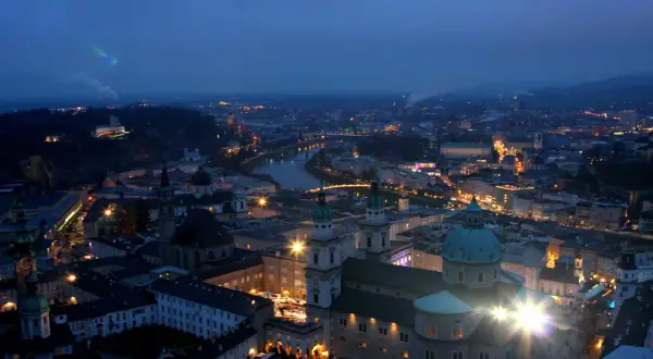 Salzburg im Winter bei Nacht. Lichter der Stadt, die Salzach und die Festung Hohensalzburg erhellen die Szene.