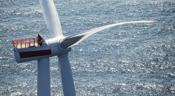 Ogromna turbina wiatrowa na morzu, symbol nowoczesnej morskiej energetyki wiatrowej, obraca łopatami na tle błyszczącej wody.