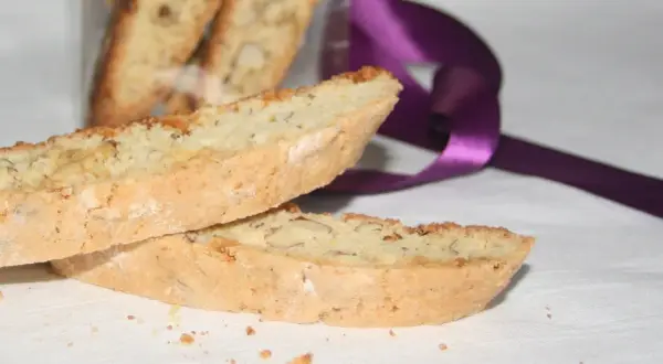 Två mandelkakor, perfekta för ditt biscotti recept, ligger på en vit duk. En lila sidenband ligger bakom.