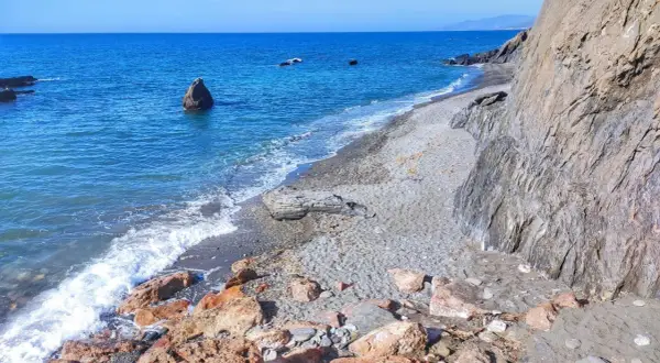 Costa de Almería, con sus guainos y rocas, el mar azul y las olas rompiendo en la playa de guijarros.