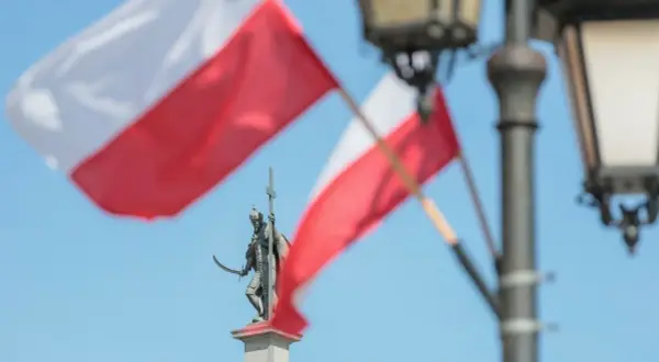 Pomnik rycerza z mieczem i krzyżem na tle polskich flag i latarni.