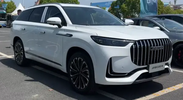 Biały SUV Jaecoo J9 z chromowanym grillem i czarnymi felgami stoi na parkingu.