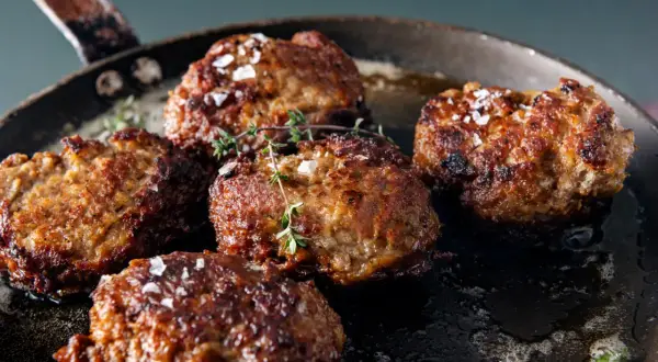 Saftige vegetarische Frikadellen braten in einer Pfanne, bestreut mit grobem Salz und frischem Thymian.