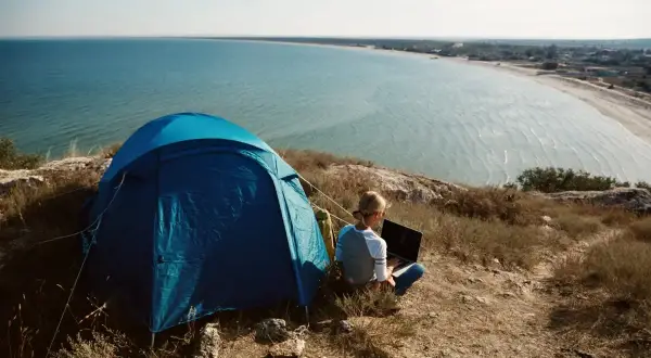 Niebieski namiot i osoba z laptopem na wzgórzu, z widokiem na morze i wybrzeże. Idealne miejsce na camping na Lazurowym Wybrzeżu.