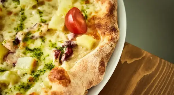 Pyszna pizza z kawałkami ananasa, ośmiornicy i pomidorkiem, obficie posypana zielonym pesto i roztopioną **mozzarellą w bloku**.