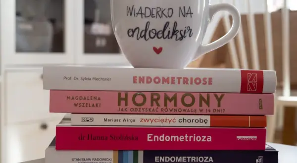 Stos książek o endometriozie, w tym "Endometrioza: diagnostyka i leczenie", z kubkiem "Wiaderko na endoeliksir".