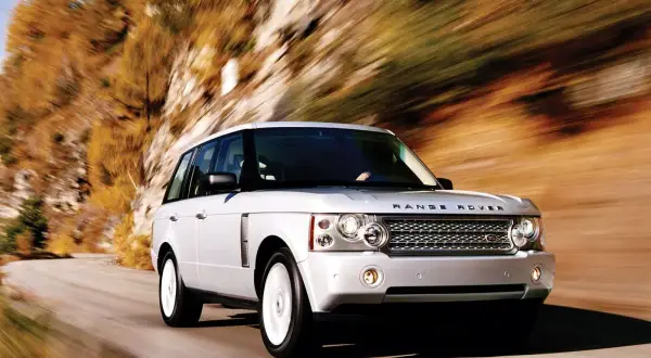 Biały Range Rover L322 pędzi po krętej drodze wśród jesiennych drzew.