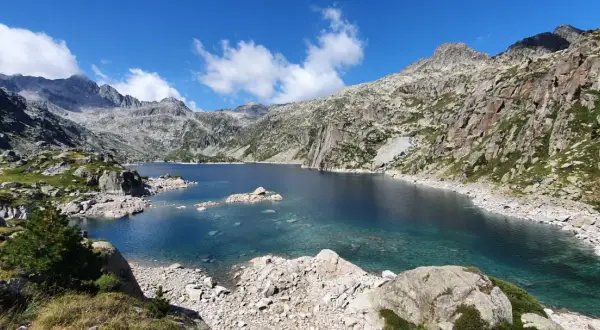 Lago azul cristalino en el corazón del Vall de Boí Aigüestortes, rodeado de imponentes montañas rocosas y vegetación escasa.