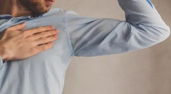 Hombre con camisa azul mostrando manchas de sudor bajo el brazo. Una solución para quitar manchas de sudor es necesaria.
