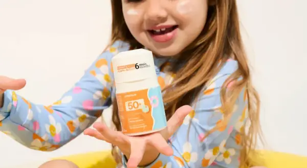 Un enfant tient un flacon de crème solaire UVA UVB 50+. La crème est conçue pour les enfants dès 6 mois.