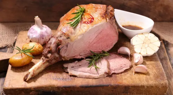 Ein saftiger Lammbraten, perfekt für Ostern, mit Rosmarin, Knoblauch und kleinen Kartoffeln auf einem Holzbrett.