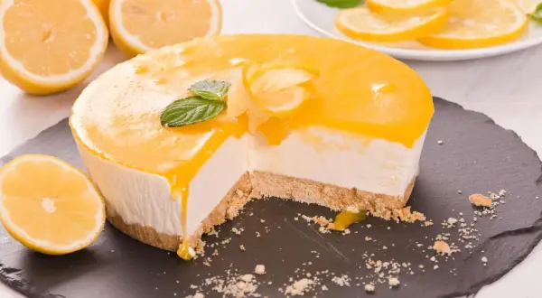 Ein Anschnitt eines cremigen Lemon Cheesecake mit Zitronenscheiben und Minze garniert.
