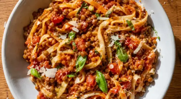 En skål med vegetarisk pasta med linser, tomatsås och basilika, toppad med riven ost.