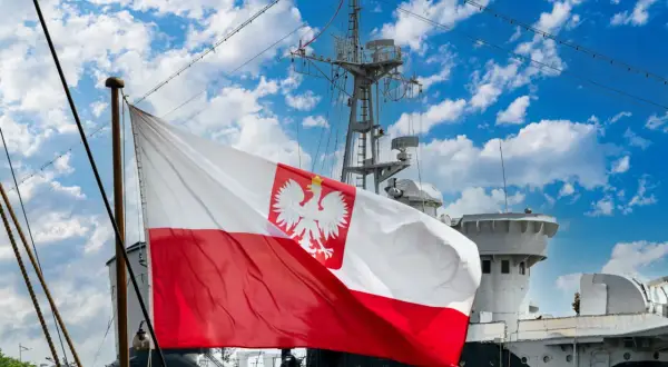 Flaga bandery z orłem dumnie powiewa na tle błękitnego nieba z chmurami, nad pokładem statku.