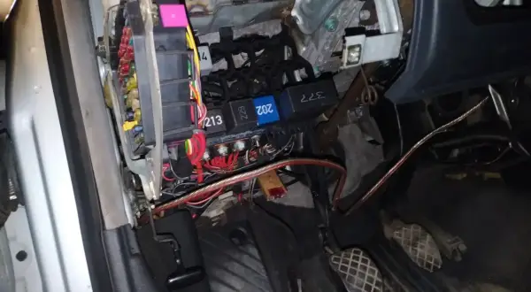 Widok na skrzynkę z bezpiecznikami i przekaźnikami w Audi A4 B6. Widać kolorowe bezpieczniki i wiązki przewodów.