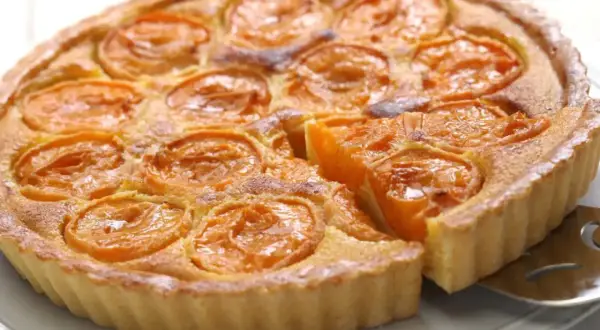 Une délicieuse tarte aux abricots, avec une part déjà servie, révèle sa garniture dorée et ses fruits juteux.