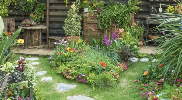 Un jardín exuberante y colorido, con flores vibrantes, follaje verde y un camino de piedras. El mantenimiento de jardinería es clave para esta belleza.