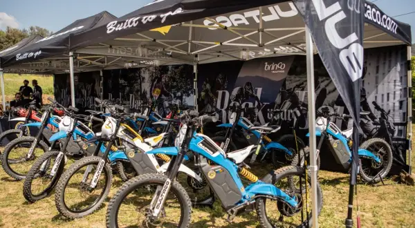 Varias motocicletas Bultaco Brinco eléctricas, de colores azul y blanco, expuestas bajo una carpa.