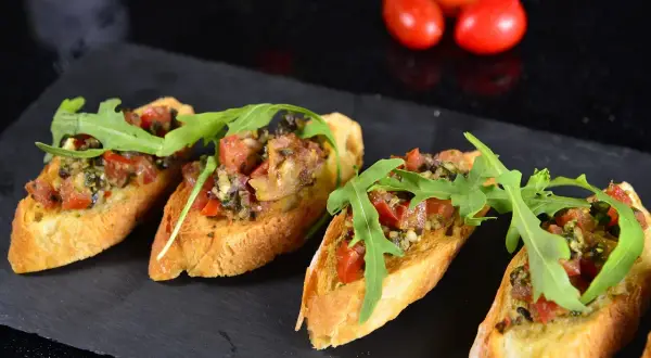 Hiszpańskie tapas kanapeczki z pomidorami, rukolą i ziołami, ułożone na czarnym kamieniu.