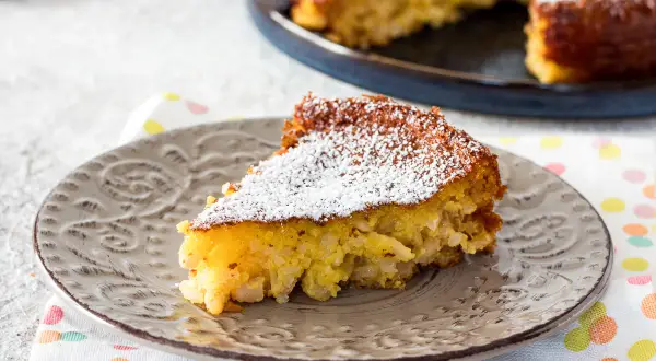 Una fetta di torta di riso, la ricetta della nonna, cosparsa di zucchero a velo su un piatto grigio.