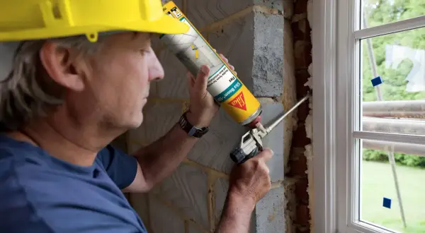 Obrero con casco amarillo aplica espuma expansiva para sellar ventanas exterior.