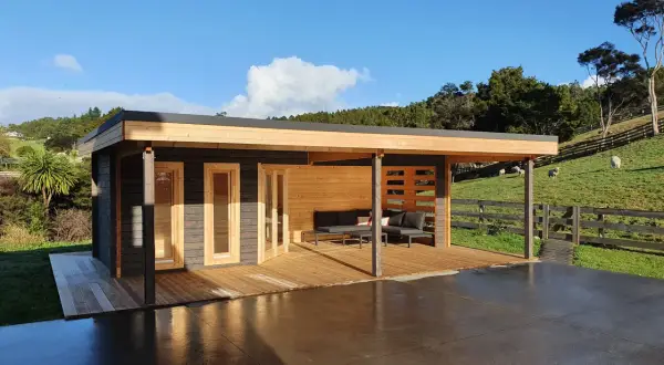 Modern cabin with porches cerrados de obra, deck, and outdoor seating, set against a green hillside with sheep.