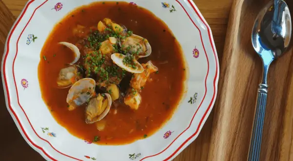 En skål med bouillabaisse med musslor och räkor, perfekt att servera med ett glas vin.